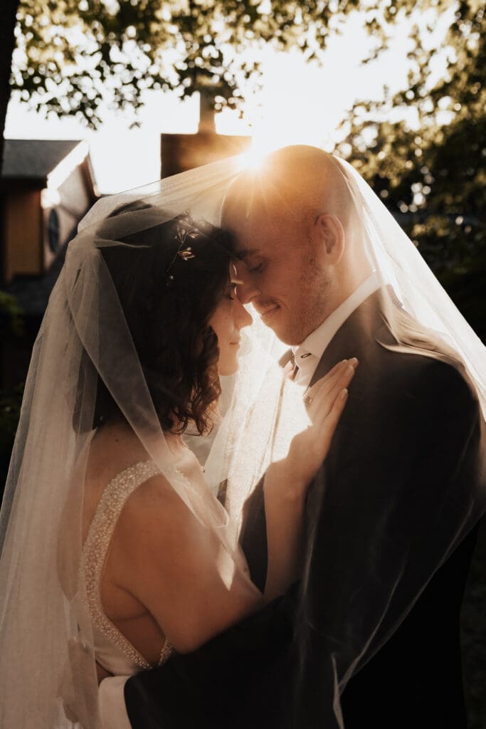A wedding photo with a couple embraced in each other's arms and a sunflare peaking over top of them.